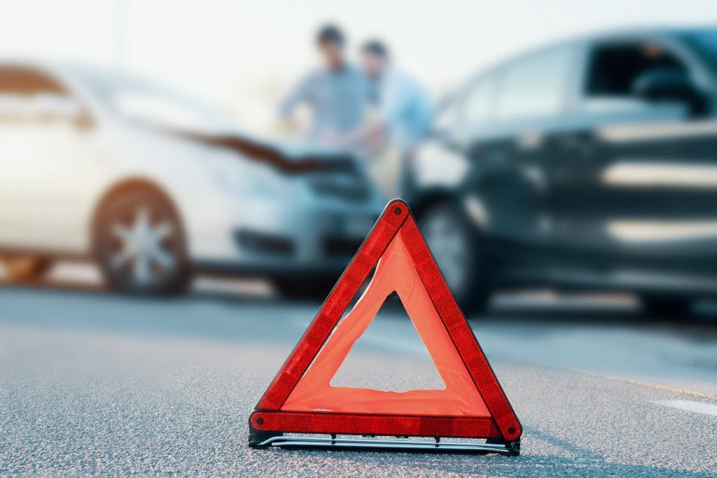 Yellow hazard triangle in front of two cars in auto accident insurance claim